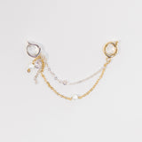 A delicate double-layered chain earring accessory featuring a gold chain with a small pearl bead and a silver chain with a clear rhinestone, attached to a gold and silver hoop earring on a light gray background.