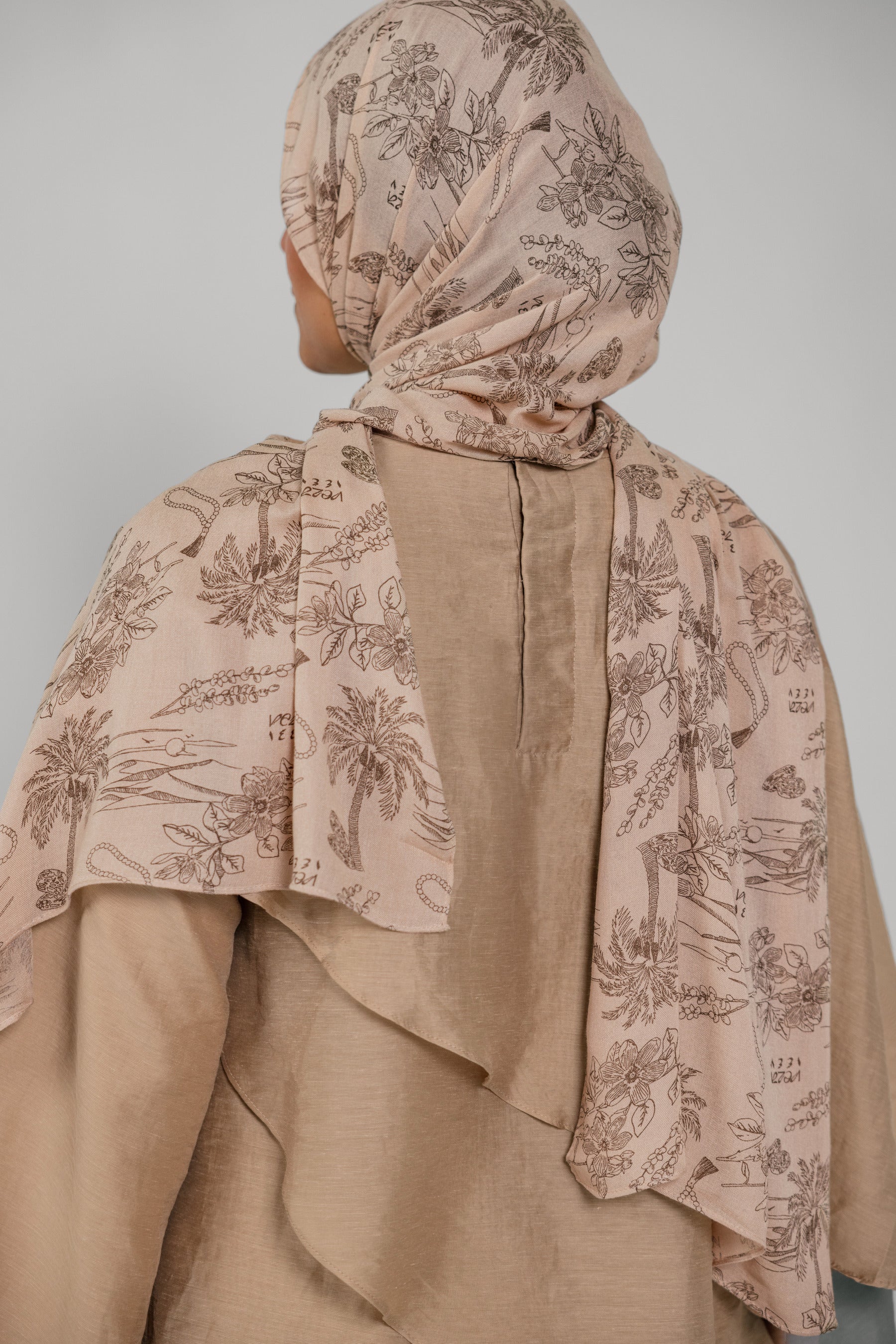 Person wearing a beige hijab with floral patterns against a plain background