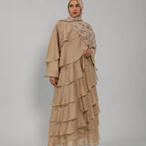Woman wearing a beige layered dress and hijab on a gray background