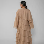 Woman wearing a beige ruffled dress and hijab on a gray background