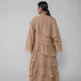 Woman wearing a beige ruffled dress and hijab on a gray background