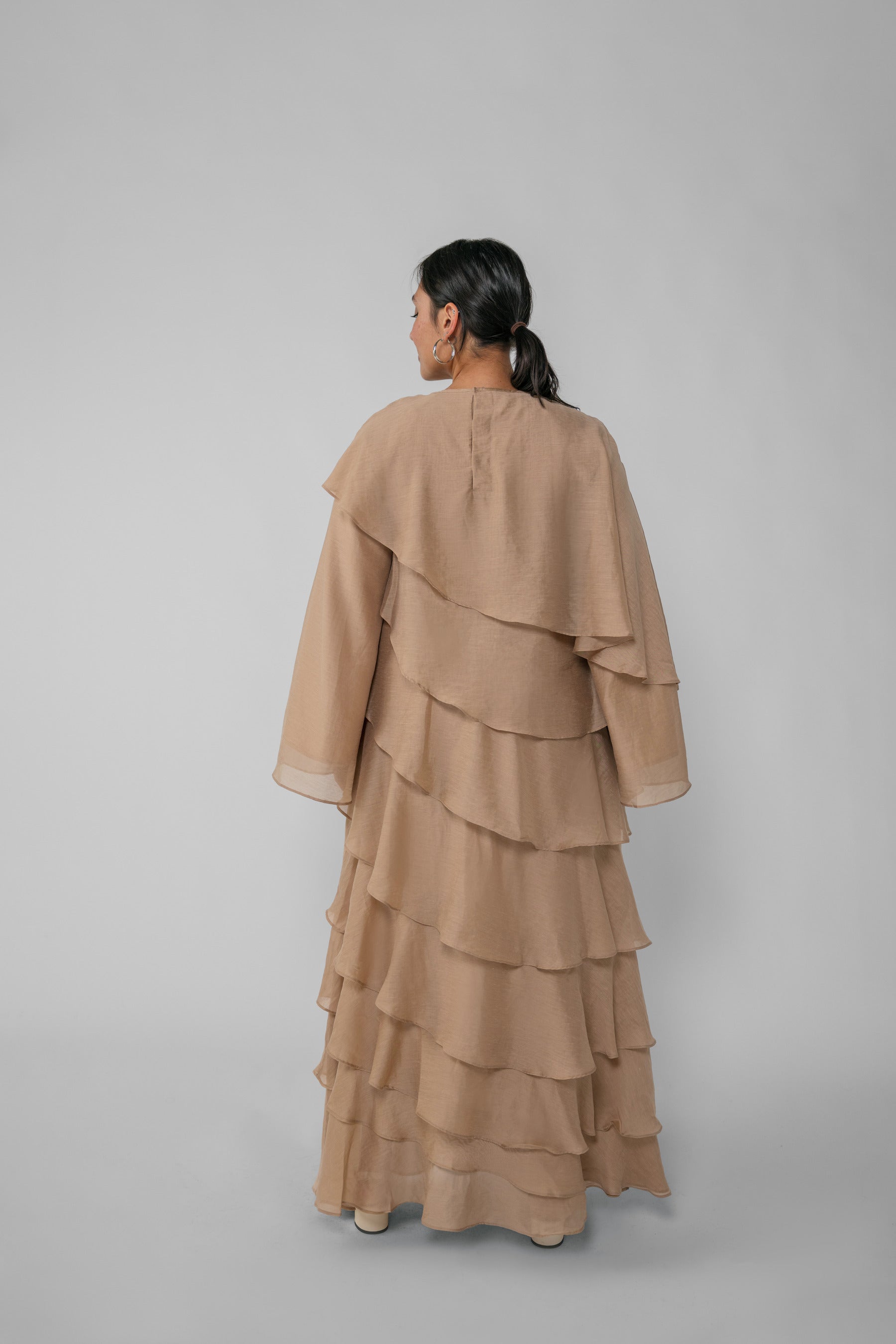 Woman wearing a beige ruffled dress and hijab on a gray background