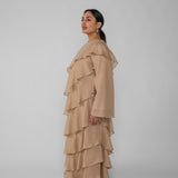 Woman wearing a beige ruffled dress and hijab on a gray background