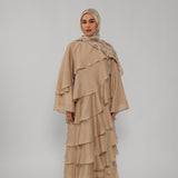 Woman wearing a beige layered dress and hijab on a gray background