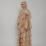 Woman wearing a beige ruffled dress and hijab on a gray background