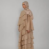 Woman wearing a beige ruffled dress and hijab on a gray background