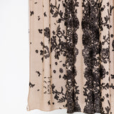 Close-up of a sheer beige mesh fabric with vertical black floral lace panels and scattered black floral motifs, shown against a plain white background.