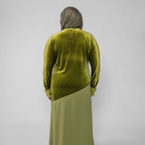 Person wearing a green velvet top and matching long skirt on a gray background