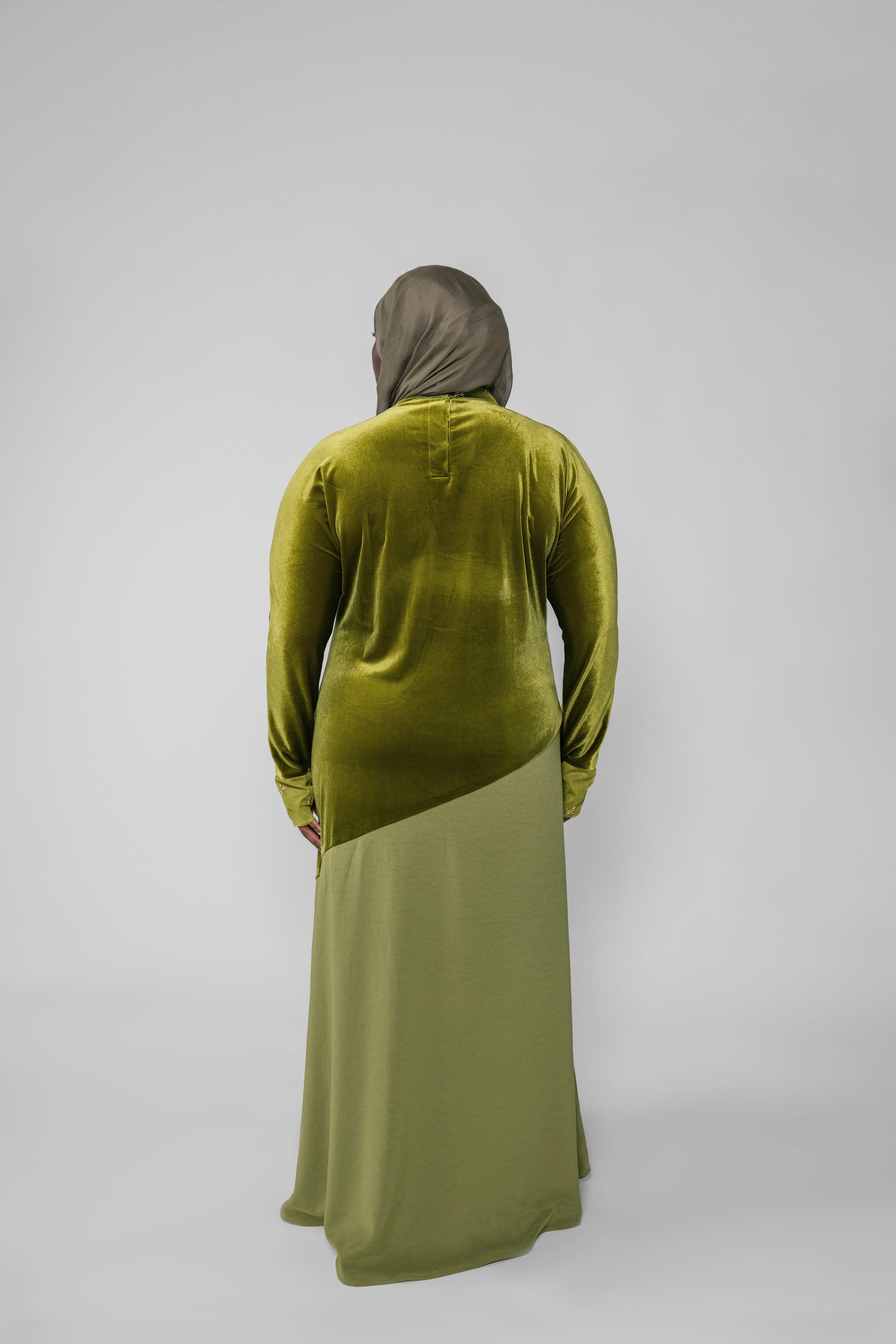 Person wearing a green velvet top and matching long skirt on a gray background