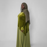 Woman wearing a green dress and headscarf against a white background