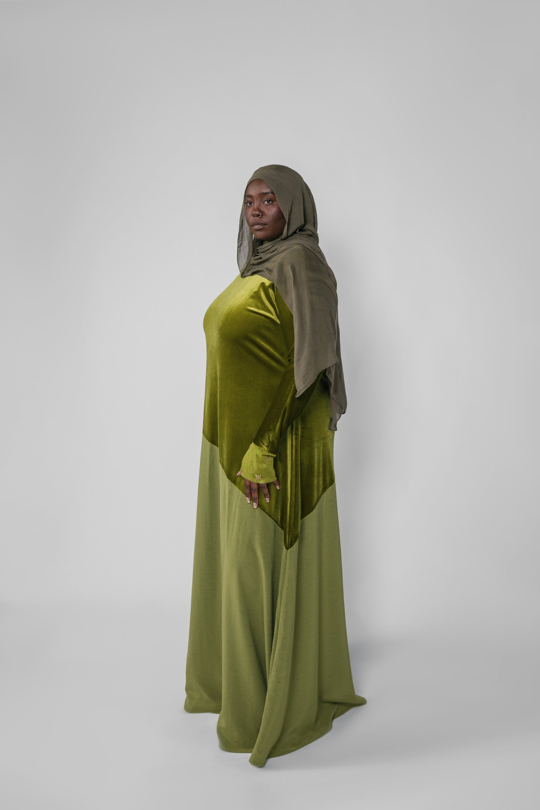 Woman wearing a green dress and headscarf against a white background