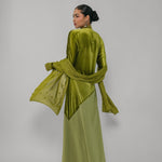 Woman wearing a green velvet outfit with a matching scarf on a plain background