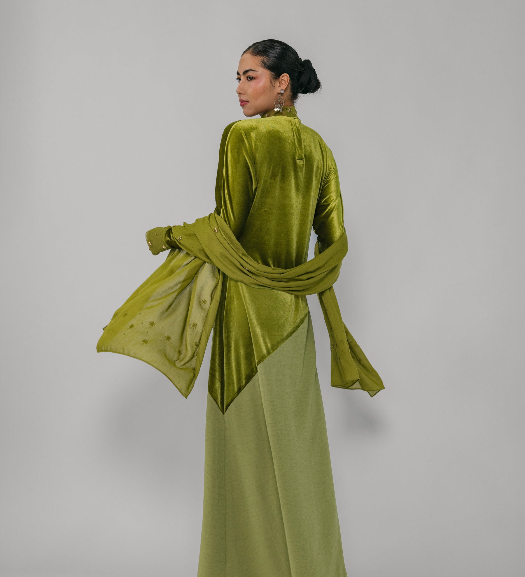 Woman wearing a green velvet outfit with a matching scarf on a plain background