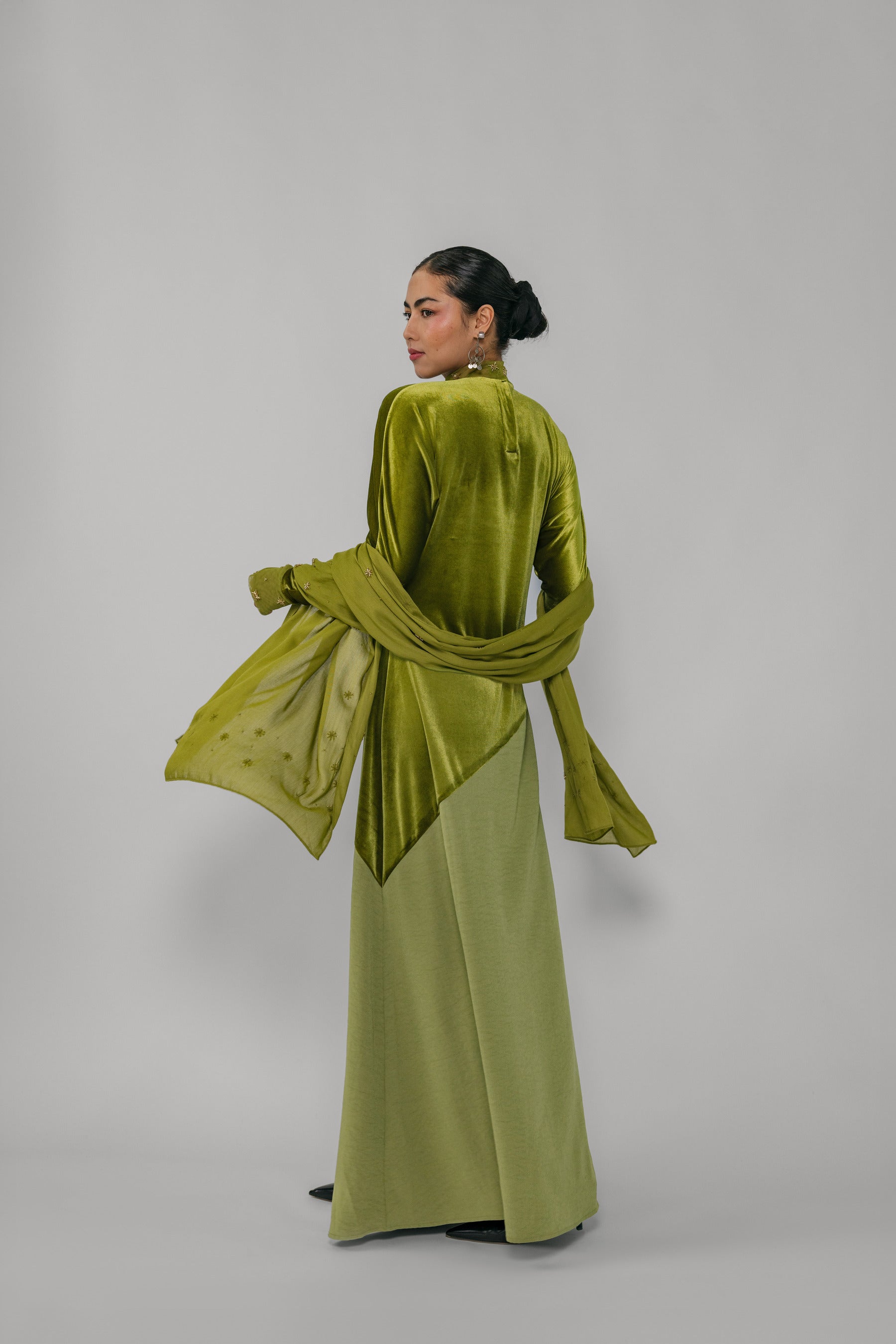 Woman wearing a green velvet outfit with a matching scarf on a plain background