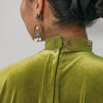 Green velvet garment with decorative collar and earrings on a neutral background