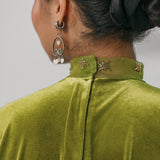 Green velvet garment with decorative collar and earrings on a neutral background