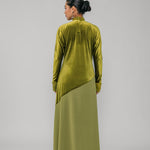 Person wearing a green velvet outfit with a long skirt on a gray background