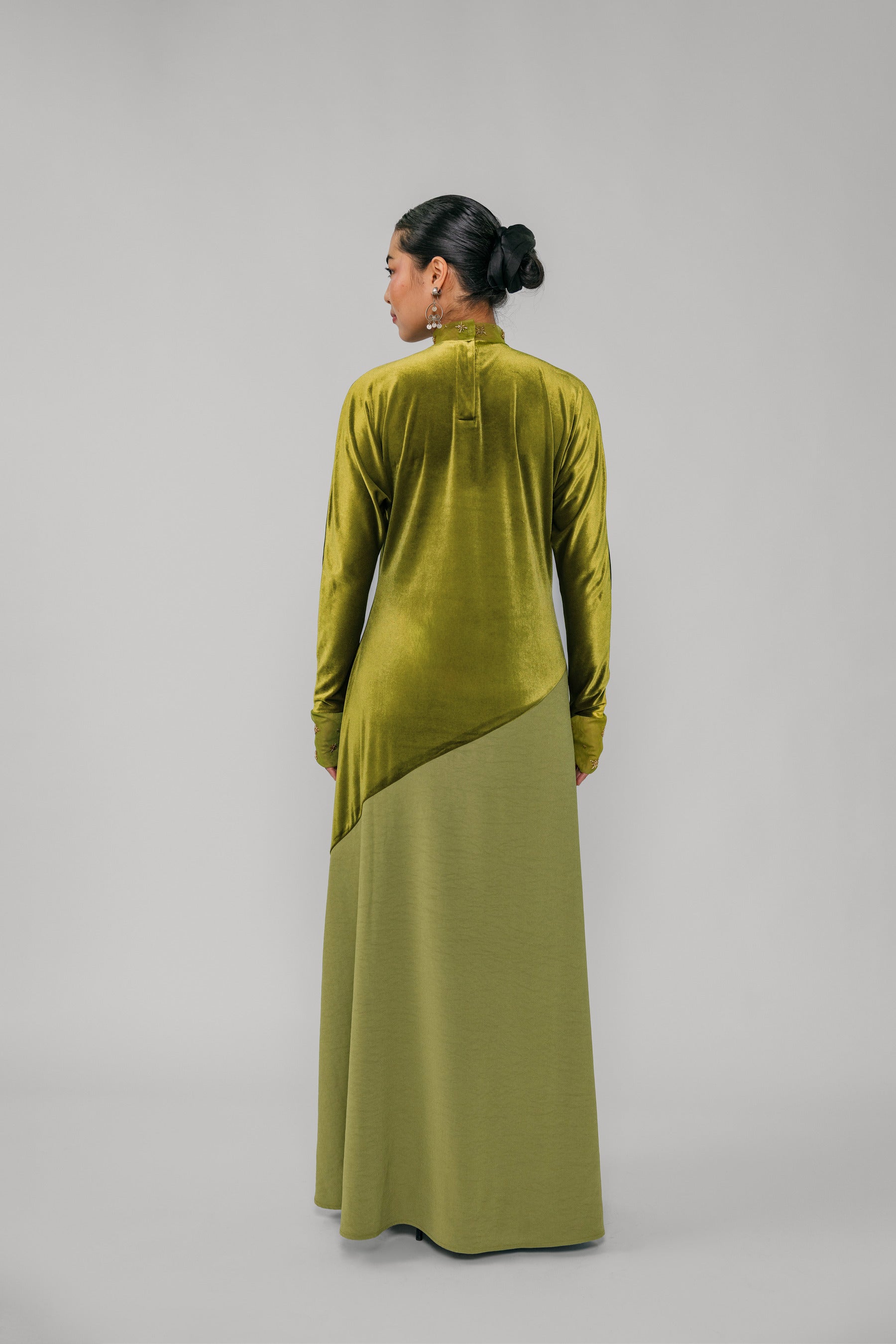 Person wearing a green velvet outfit with a long skirt on a gray background