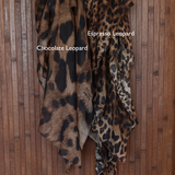 Print comparison of two leopard print hijabs labeled 'Chocolate Leopard' and 'Espresso Leopard' on a wooden background.