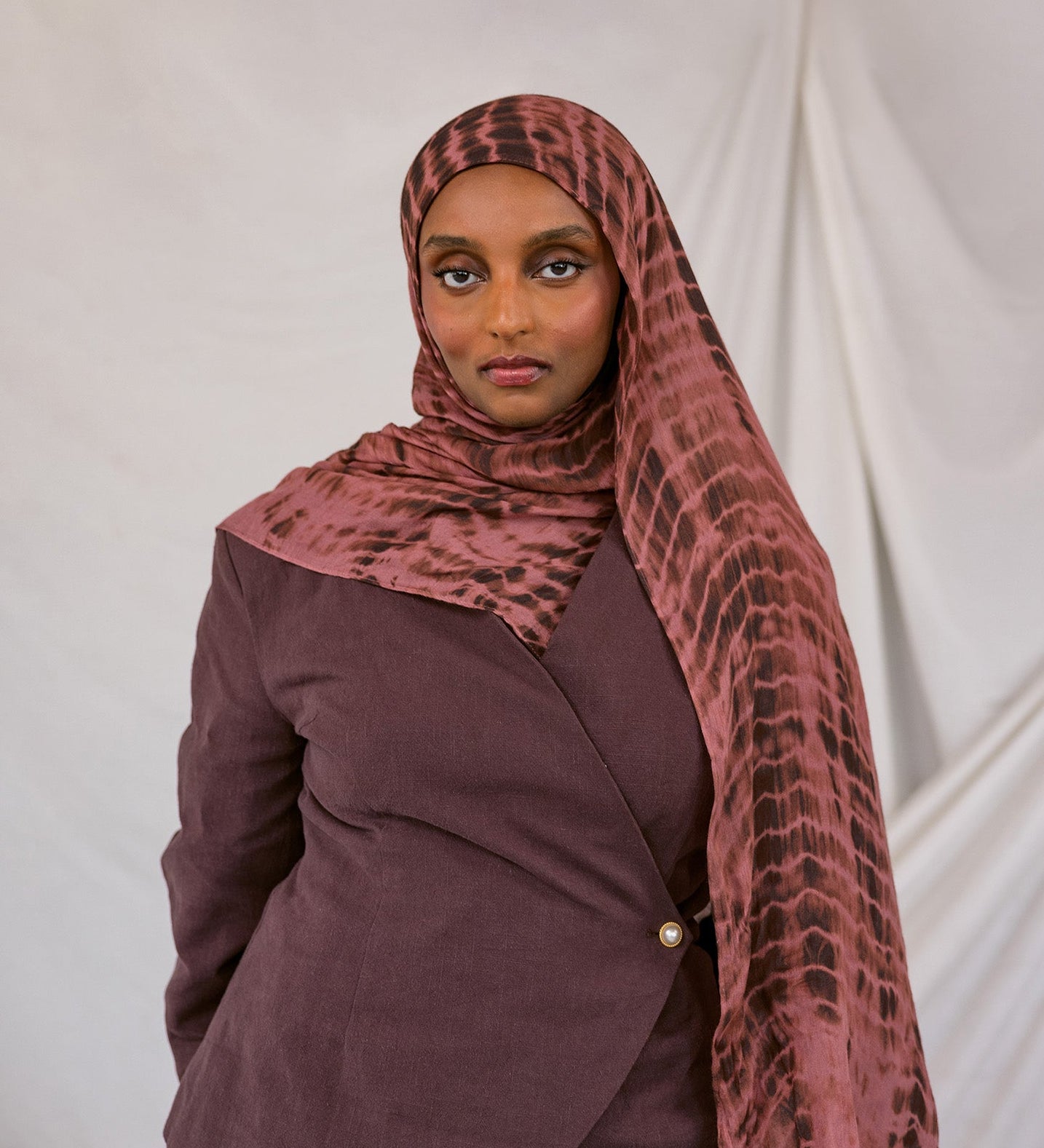 Woman wearing a red clay ripple print hijab and jacket against a white background