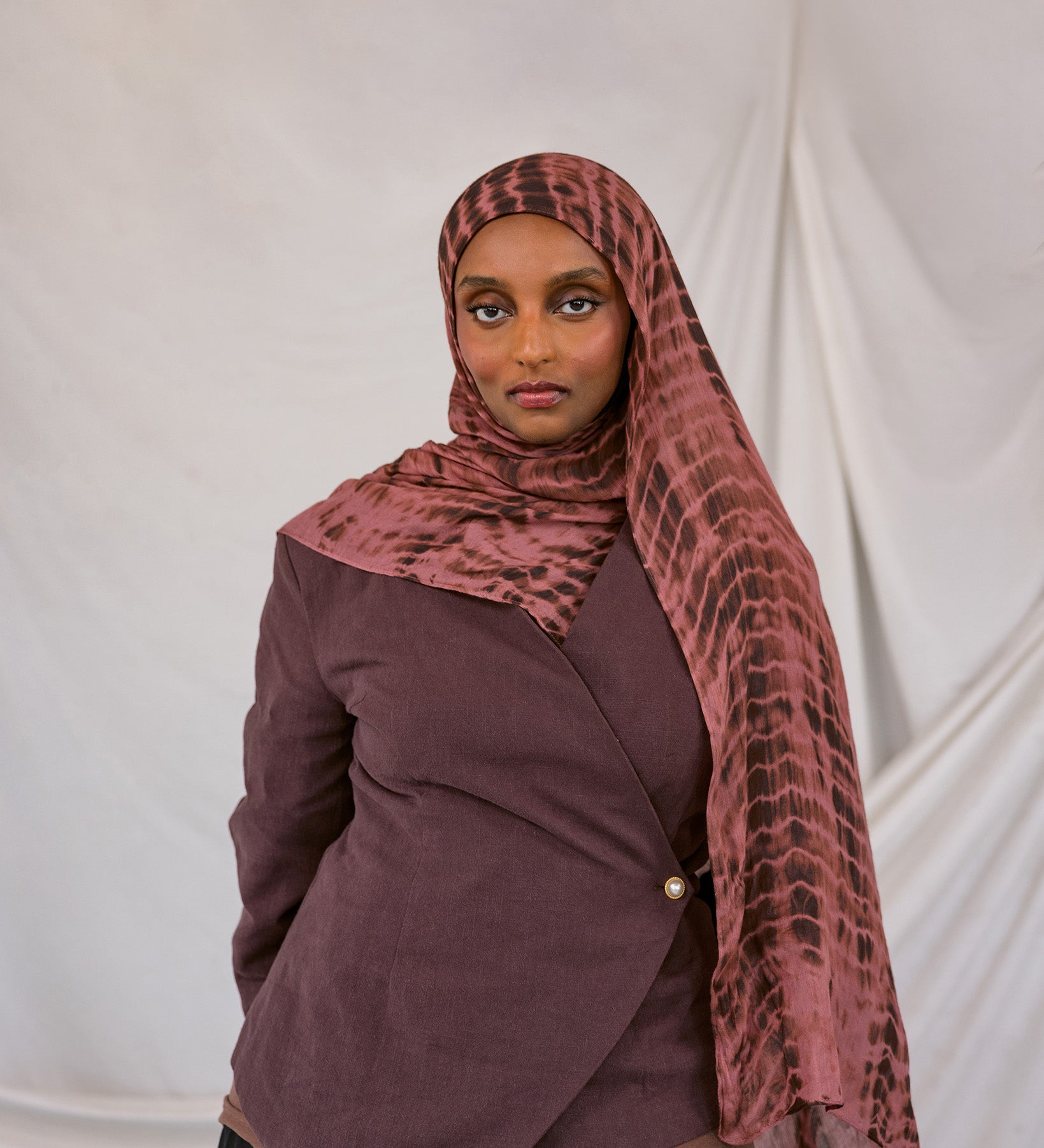 Woman wearing a red clay ripple print hijab and jacket against a white background