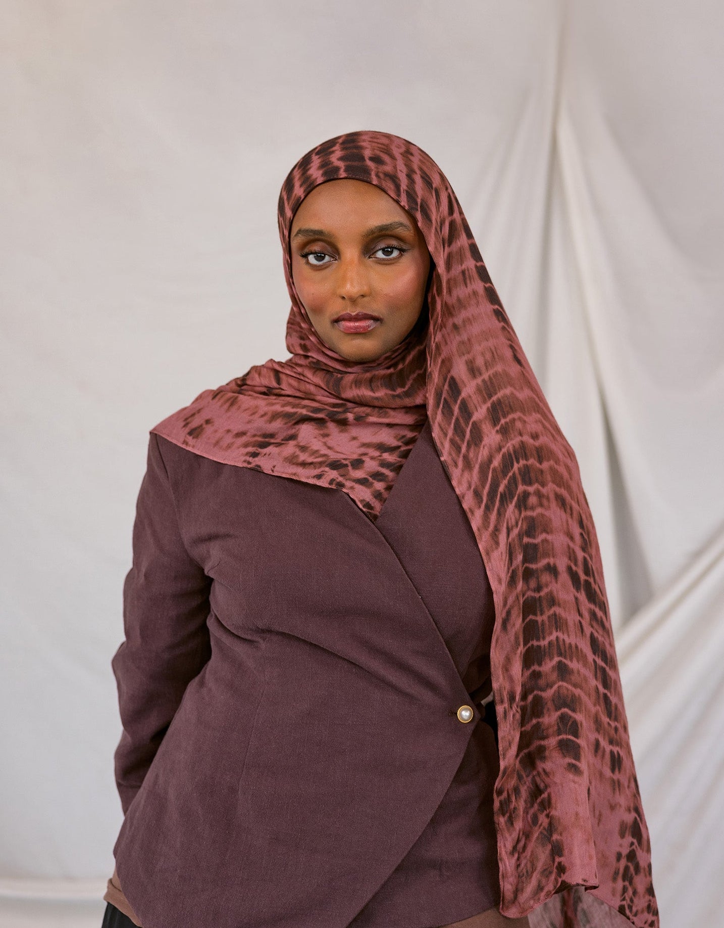 Woman wearing a red clay ripple print hijab and jacket against a white background
