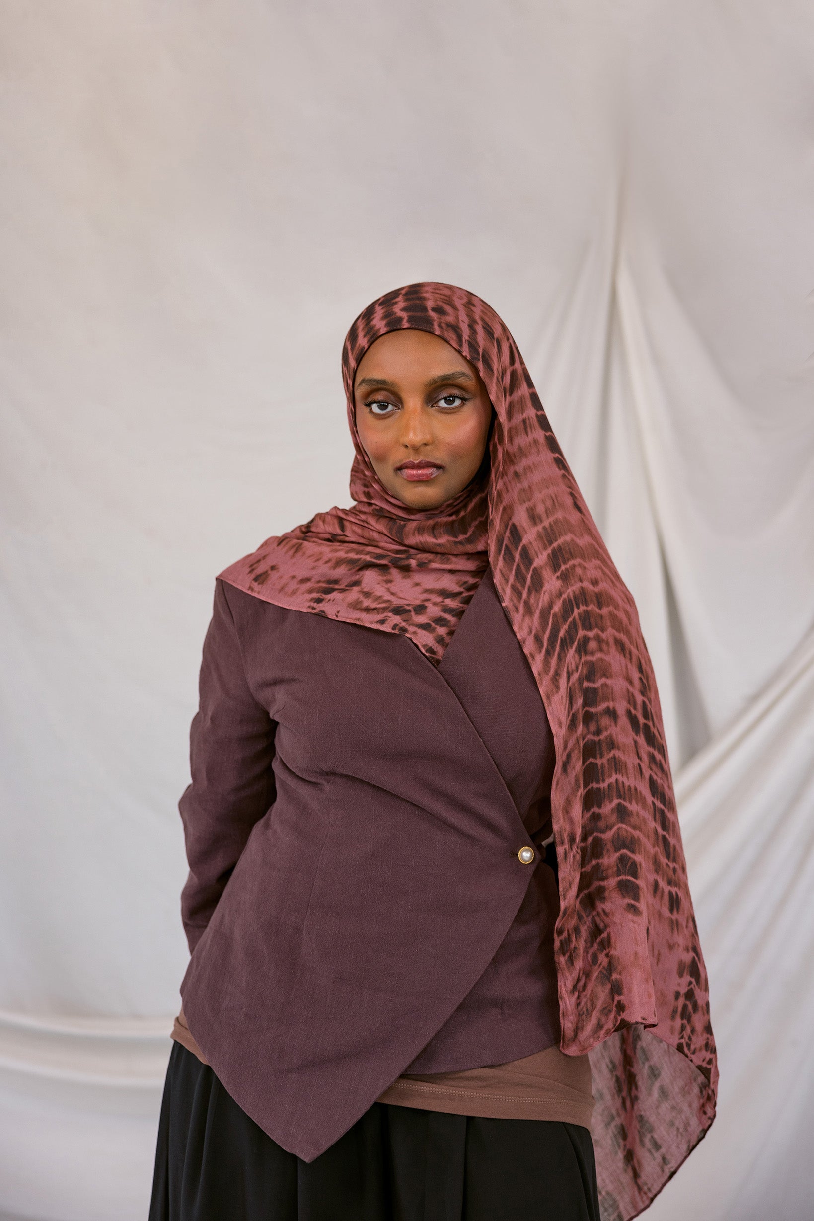 Woman wearing a red clay ripple print hijab and jacket against a white background