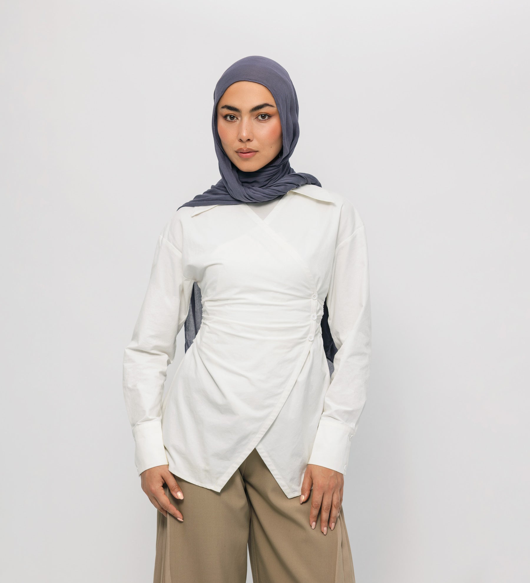 Woman wearing a white long-sleeve top and beige pants with a gray hijab on a white background