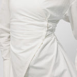Close-up of a white dress with ruched detail on a light gray background