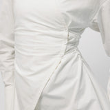Close-up of a white dress with ruched detail on a light gray background