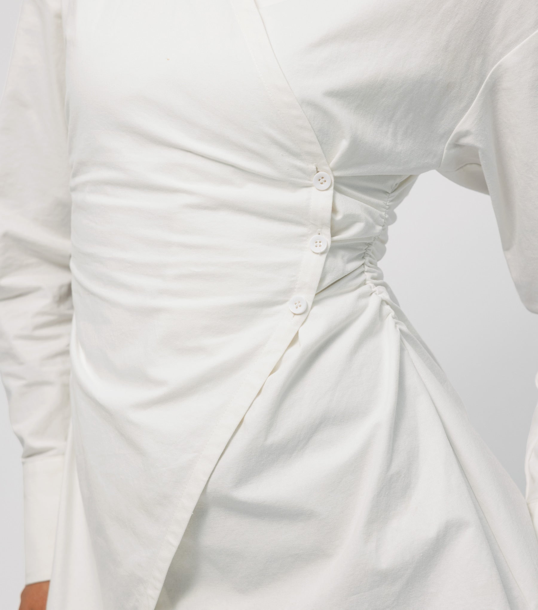 Close-up of a white dress with ruched detail on a light gray background