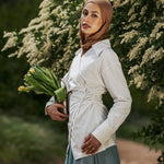 Woman in a hijab holding flowers outdoors with greenery in the background