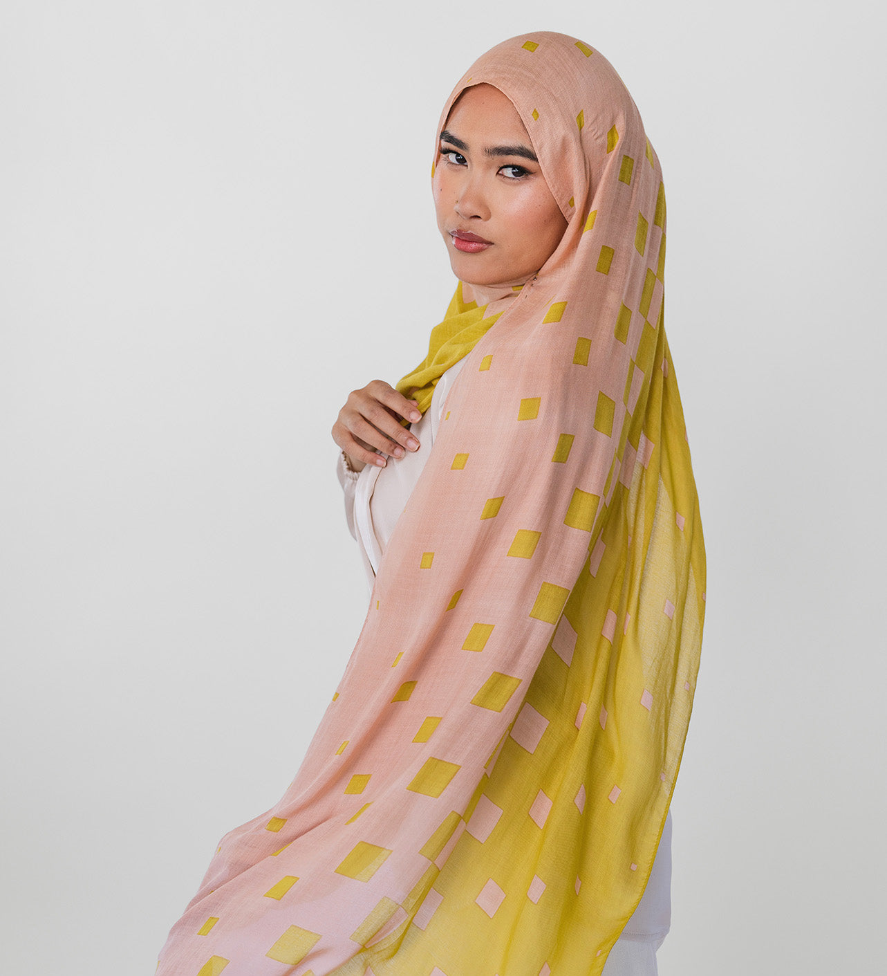 Woman wearing a pink and yellow polka dot hijab on a white background