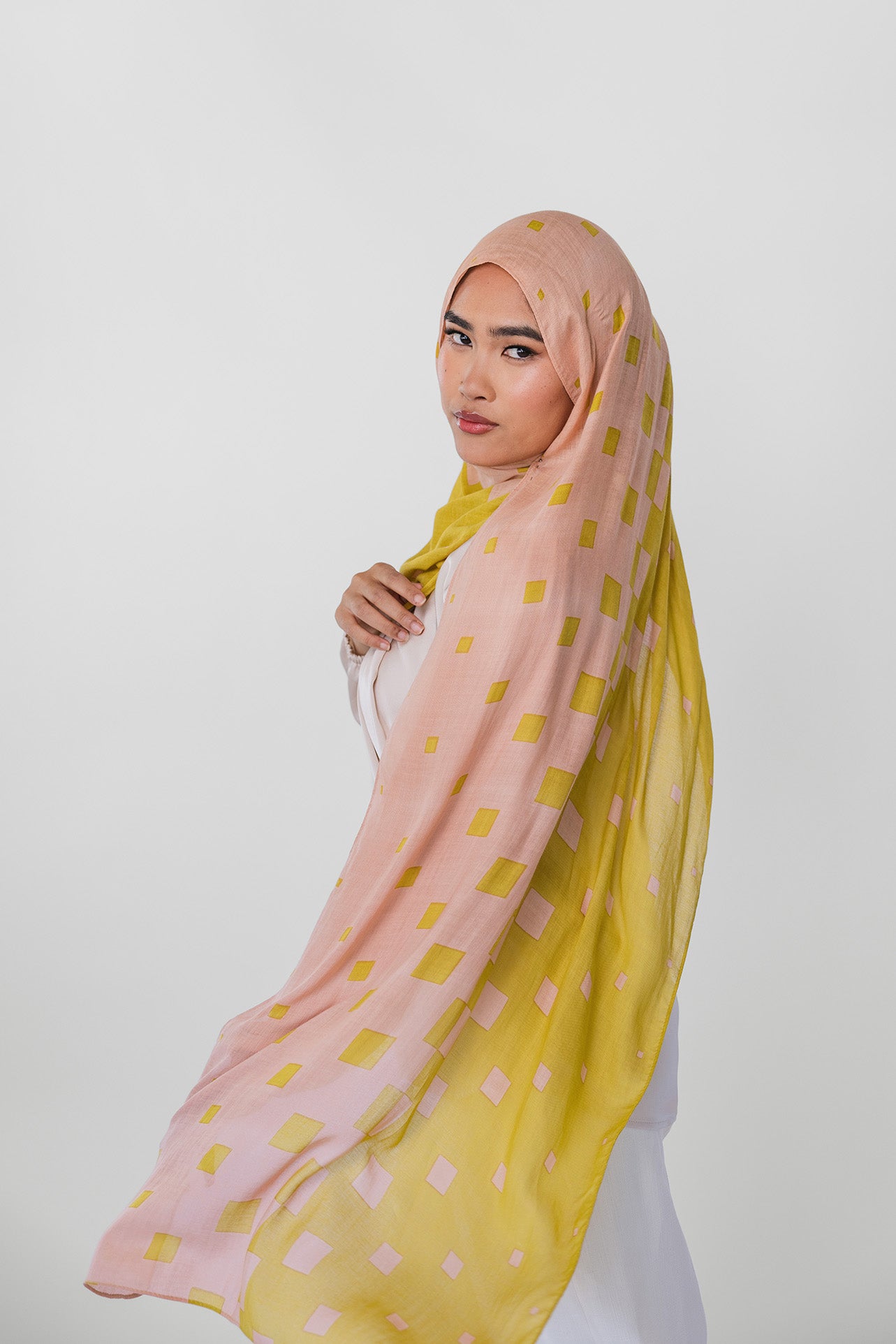 Woman wearing a pink and yellow polka dot hijab on a white background