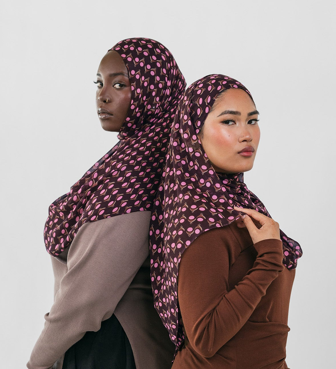 Two women wearing patterned hijabs against a white background