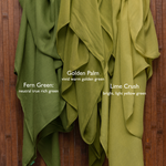 Three green scarves labeled 'Fern Green',  'Lime Crush', and 'Lime Crush' on a wooden background with Vela branding.