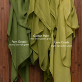 Three green scarves labeled 'Fern Green',  'Lime Crush', and 'Lime Crush' on a wooden background with Vela branding.