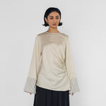 Woman wearing a beige long-sleeve top with striped cuffs and black wide-leg pants on a white background
