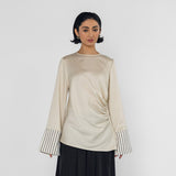 Woman wearing a beige long-sleeve top with striped cuffs and black wide-leg pants on a white background