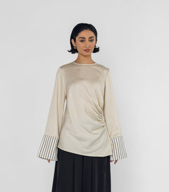 Woman wearing a beige long-sleeve top with striped cuffs and black wide-leg pants on a white background