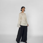 Woman wearing a beige long-sleeve top and black wide-leg pants on a white background