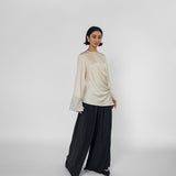 Woman wearing a beige long-sleeve top and black wide-leg pants on a white background