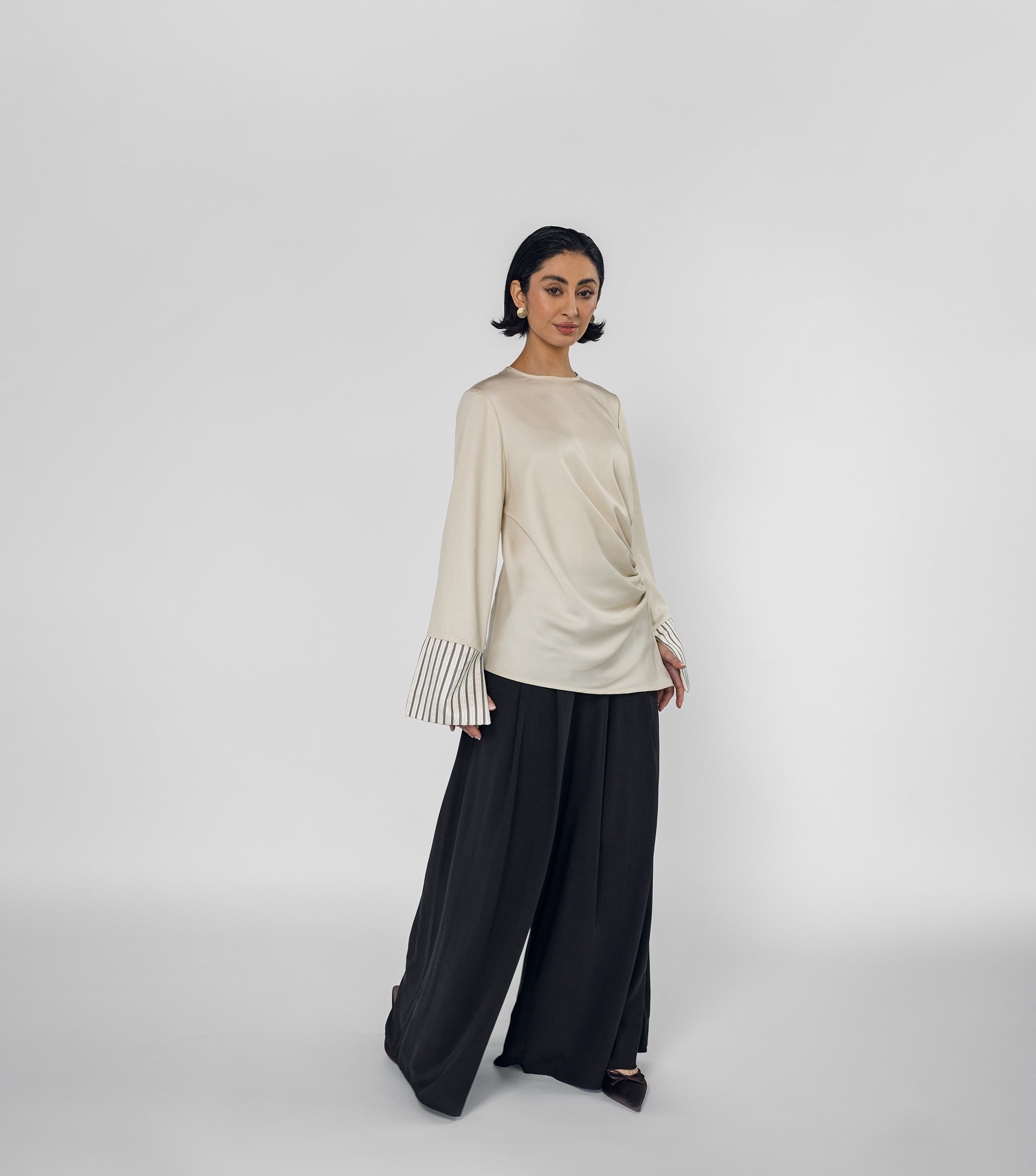 Woman wearing a beige long-sleeve top and black wide-leg pants on a white background
