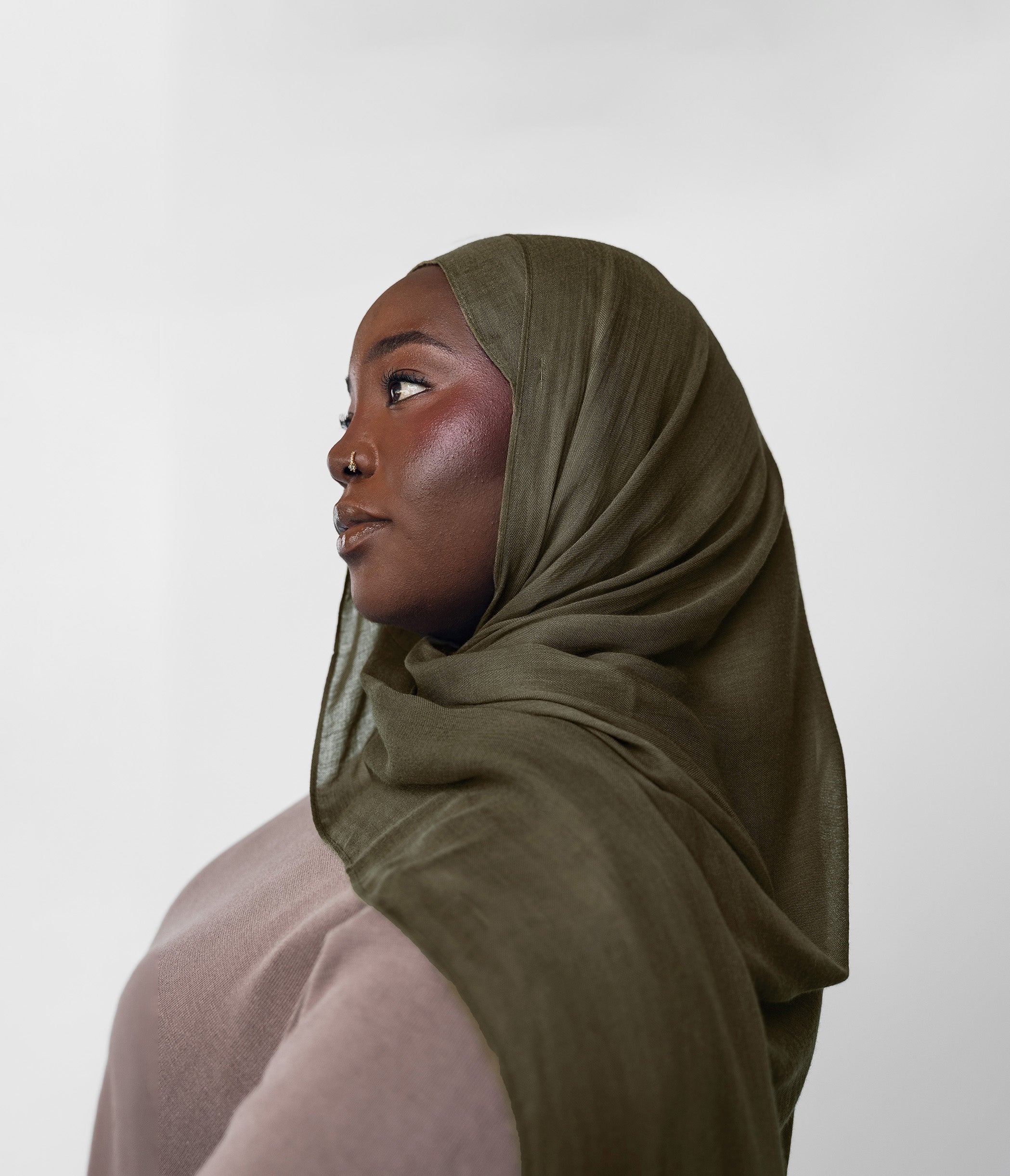 Woman wearing an olive hijab against a white background