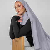 Woman wearing a light gray hijab and black top against a white background