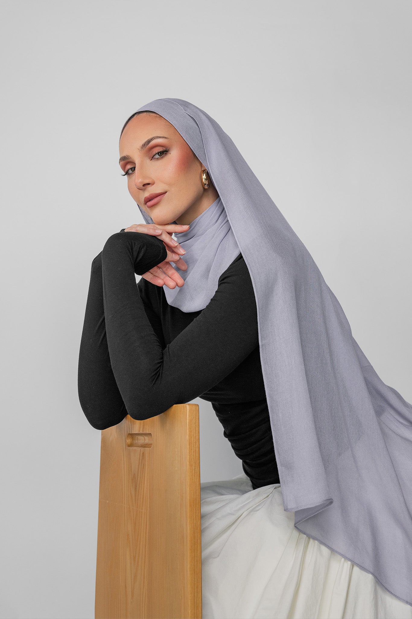 Woman wearing a light gray hijab and black top against a white background