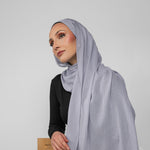 Woman wearing a light blue-gray hijab against a plain background