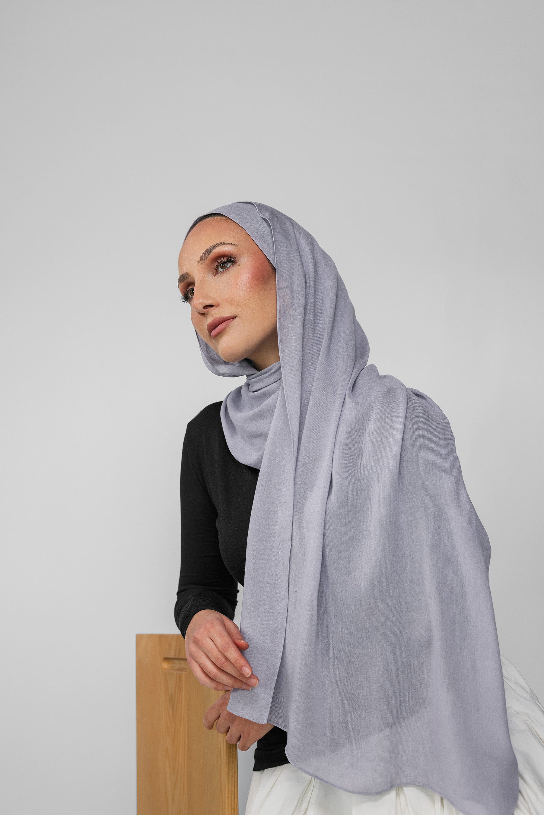 Woman wearing a light blue-gray hijab against a plain background