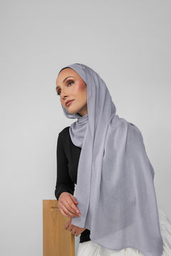 Woman wearing a light blue-gray hijab against a plain background