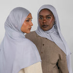 Two women wearing light blue hijabs against a white background